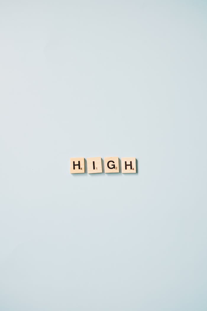 Minimalist art featuring Scrabble tiles spelling HIGH on a light blue background.